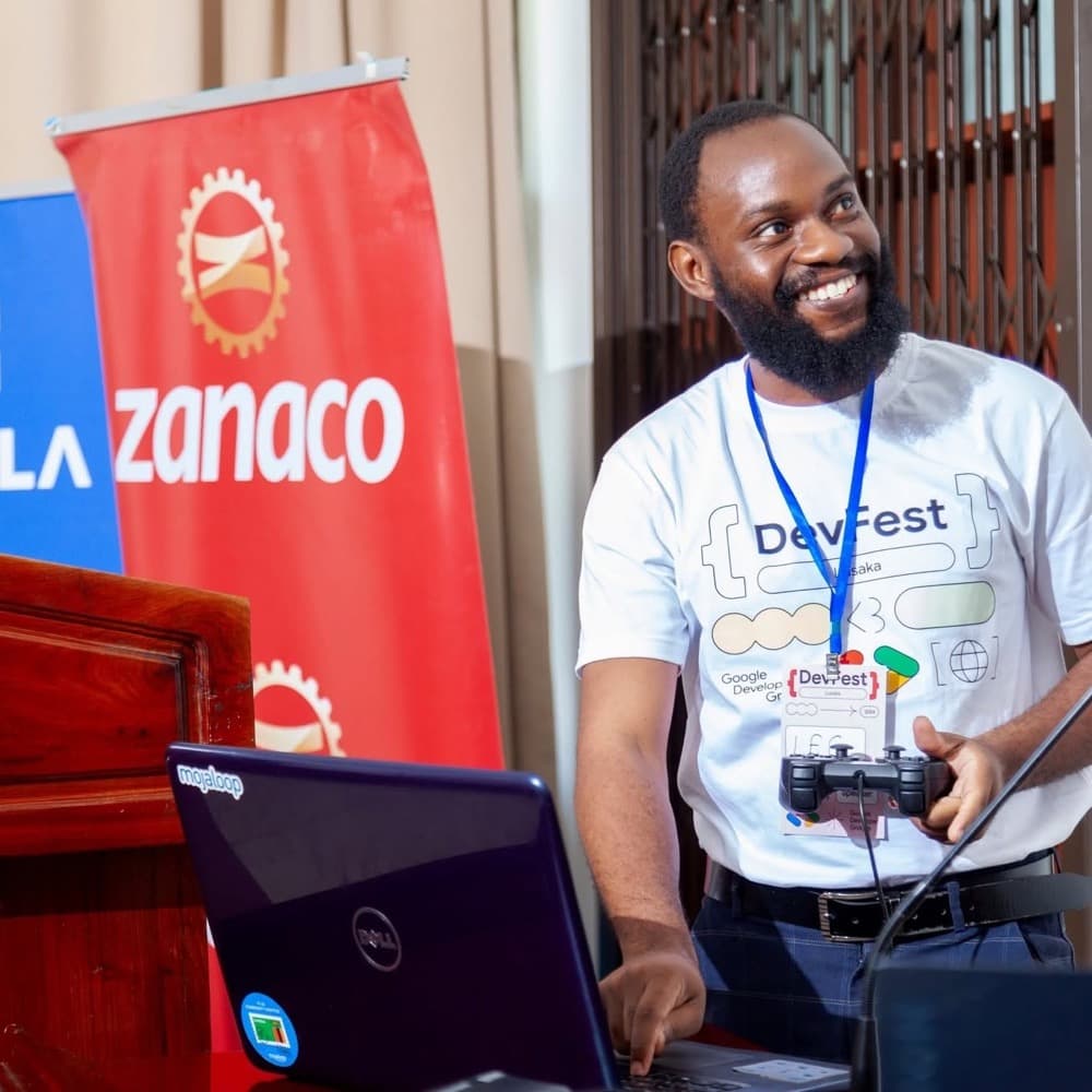 A speaker in a DevFest t-shirt smiling while presenting from a laptop